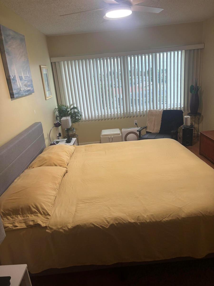 A bedroom features a king-sized bed with yellow bedding, a ceiling fan, and vertical blinds — 6670 Royal Palm Boulevard # 308k, Margate FL 33063, MARGATE, FL