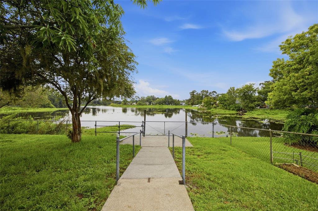 A concrete walkway leads to a fenced gate overlooking a lake surrounded by trees — 7537 HUMBOLDT AVENUE, NEW PORT RICHEY, FL