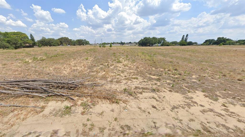 A wide, flat, sandy, and grassy vacant lot under a cloudy blue sky — 151 W 7TH STREET, FROSTPROOF, FL