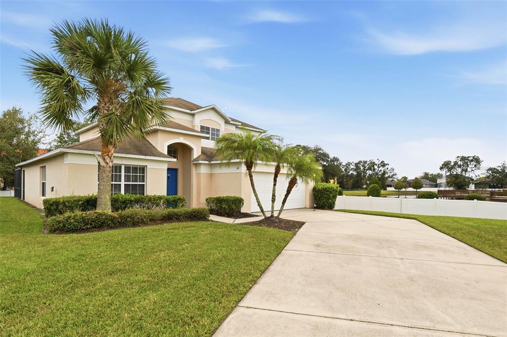 A two-story house with a beige stucco exterior, a palm tree, and a concrete driveway — 1145 SEASONS BOULEVARD, KISSIMMEE, FL