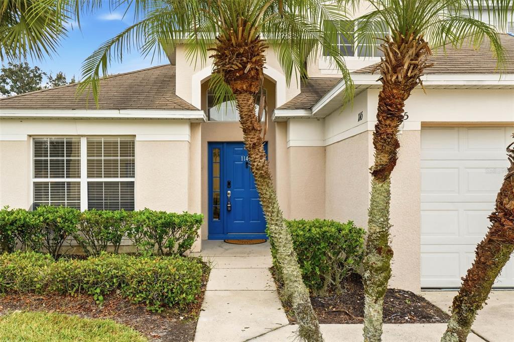 A beige house exterior features a bright blue front door and two palm trees — 1145 SEASONS BOULEVARD, KISSIMMEE, FL