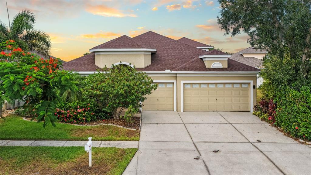 A single-story house with a three-car garage and a driveway under a sunset sky — 444 YORK DALE DRIVE, RUSKIN, FL