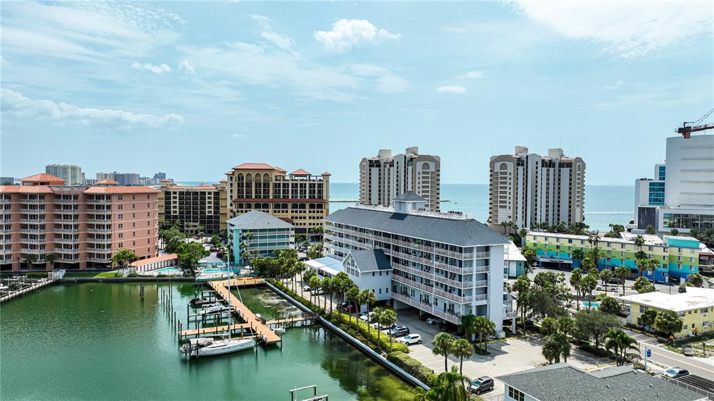An aerial view shows a coastal resort area with multi-story buildings, a marina, and boats — 445 HAMDEN DRIVE UNIT 302, CLEARWATER BEACH, FL