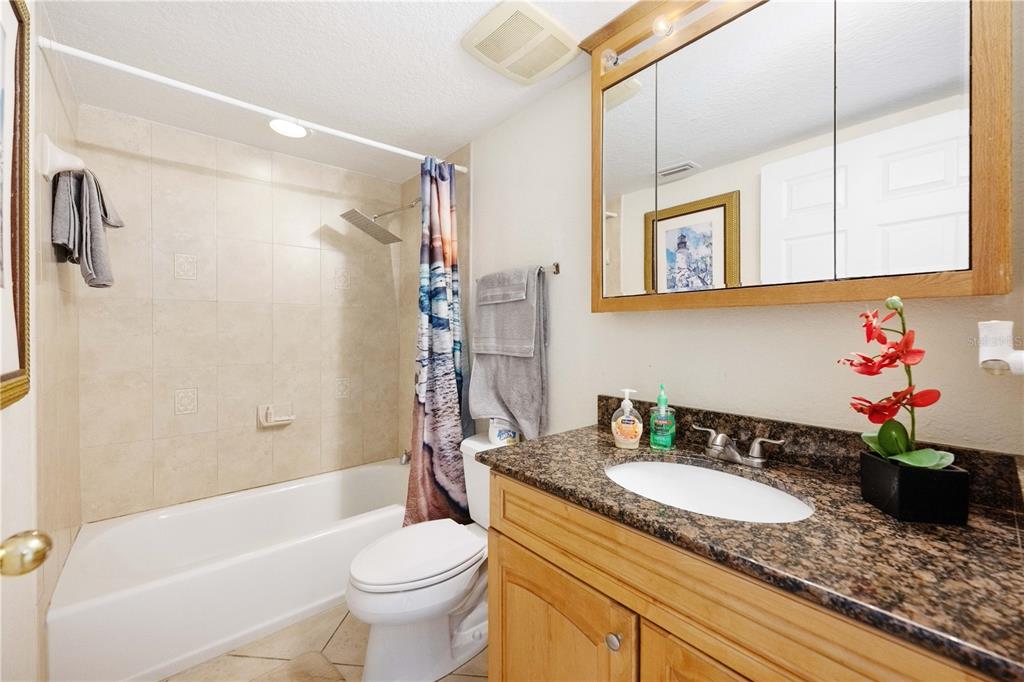 A bathroom features a granite vanity, a wooden cabinet, a toilet, and a tiled tub-shower — 445 HAMDEN DRIVE UNIT 302, CLEARWATER BEACH, FL