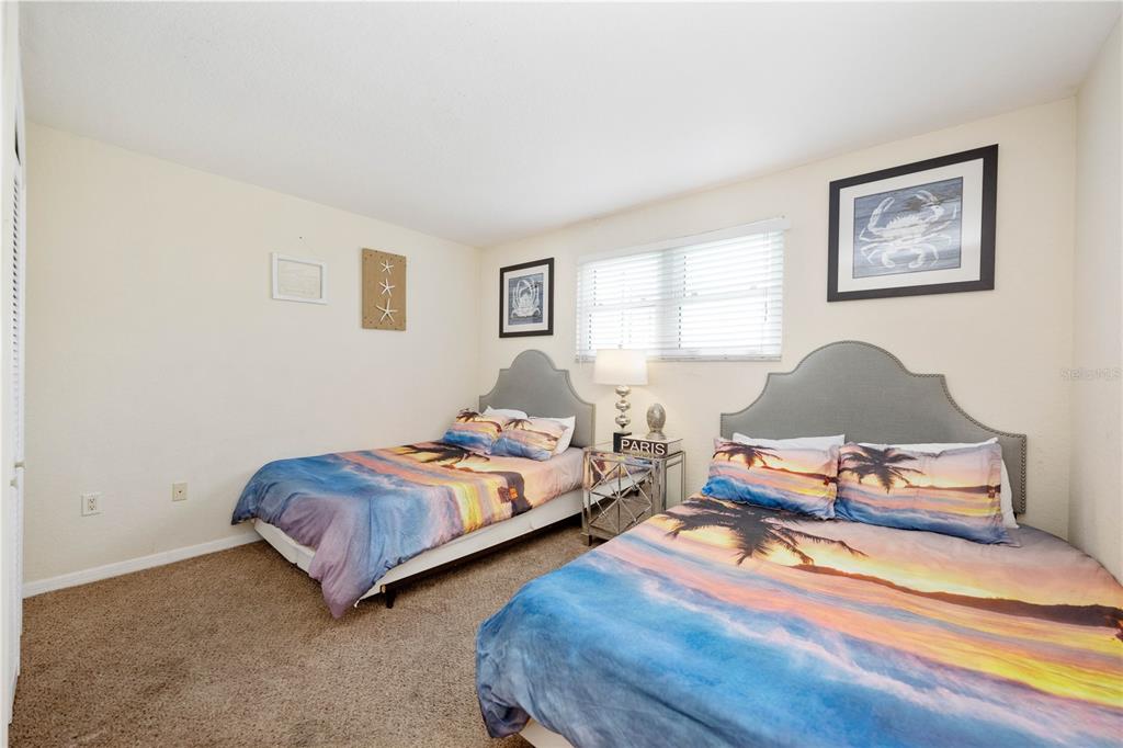 A bedroom features two beds with tropical-themed bedding, a nightstand, and framed wall art — 445 HAMDEN DRIVE UNIT 302, CLEARWATER BEACH, FL