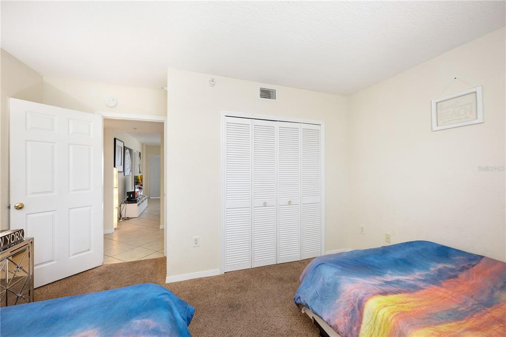 A bedroom with carpeted flooring, white walls, a closet with louvered doors, and two beds — 445 HAMDEN DRIVE UNIT 302, CLEARWATER BEACH, FL