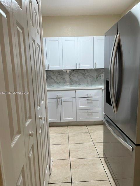 A kitchen features white cabinets, a marble-patterned backsplash, tile flooring, and a stainless steel refrigerator — 1240 NW 102nd St # 1240, Miami FL 33147, MIAMI, FL