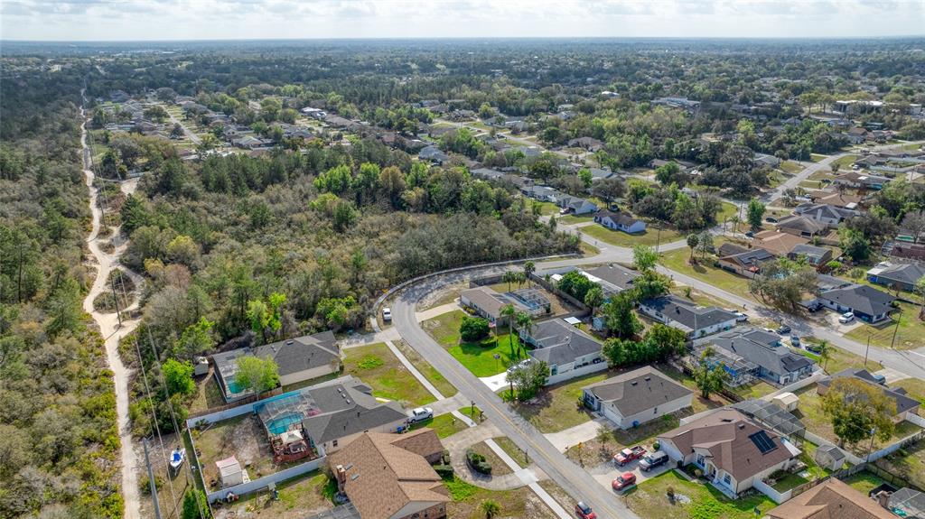 An aerial view shows a suburban neighborhood with houses, swimming pools, and surrounding wooded areas — 725 N FIRWOOD DRIVE, DELTONA, FL