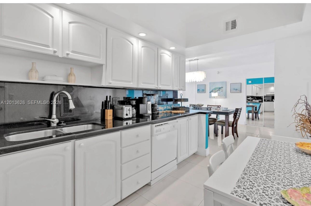 A kitchen features white cabinetry, black countertops, and a dining area in the background — 4001 S Ocean Dr # 7B, Hollywood FL 33019, HOLLYWOOD, FL