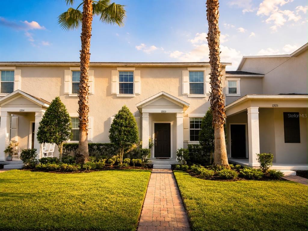 A two-story townhouse exterior with a brick walkway, palm trees, and a manicured lawn — 12820 STRODE LANE, WINDERMERE, FL