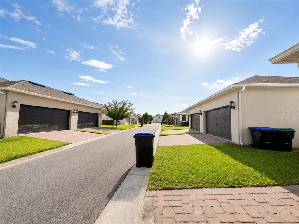 A paved residential street lined with garages, green lawns, and blue trash bins under sunlight — 12820 STRODE LANE, WINDERMERE, FL