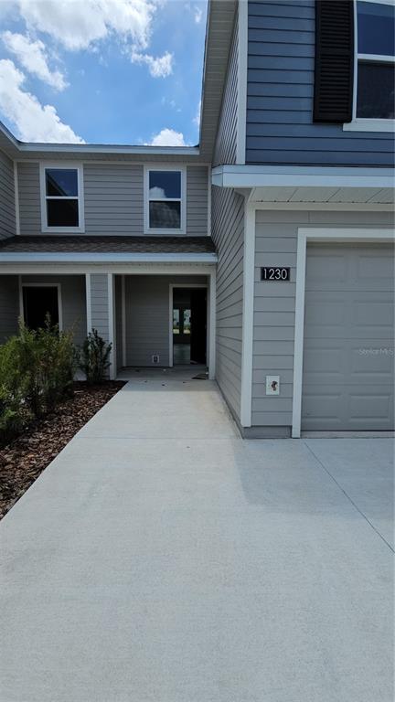 A two-story house exterior features light gray siding, a concrete driveway, and a covered entryway — 1230 ORION, DAVENPORT, FL