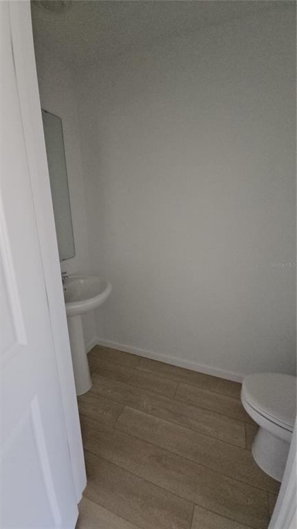 A small bathroom features a pedestal sink, a toilet, and light wood-look tile flooring — 1230 ORION, DAVENPORT, FL