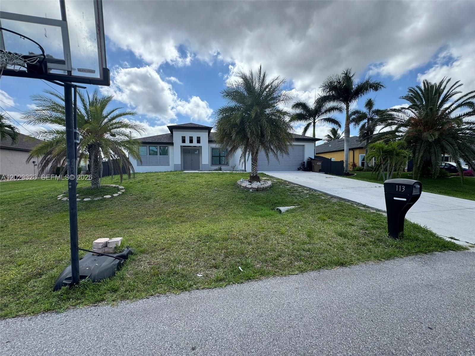 A single-story house with a white facade, palm trees, and a driveway under a cloudy sky — 113 NW 38th Pl, Cape Coral FL 33993, CAPE CORAL, FL