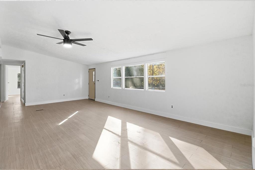 An empty room features light wood-look flooring, white walls, a ceiling fan, and three windows — 5371 W WINTER SUN LANE, HOMOSASSA, FL