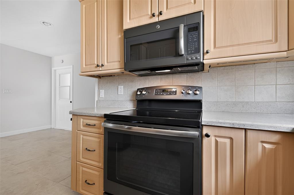 A kitchen features light wood cabinets, a black microwave, a black stove, and speckled countertops — 2221 ALEXANDER DRIVE, TITUSVILLE, FL