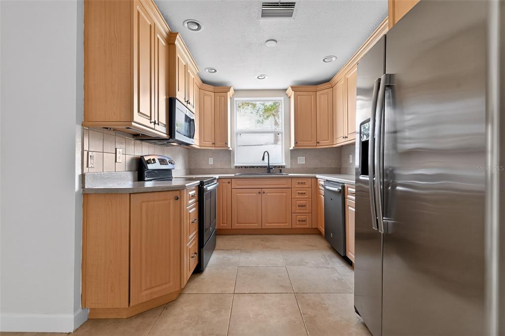 A kitchen features light wood cabinets, stainless steel appliances, and beige tile flooring — 2221 ALEXANDER DRIVE, TITUSVILLE, FL