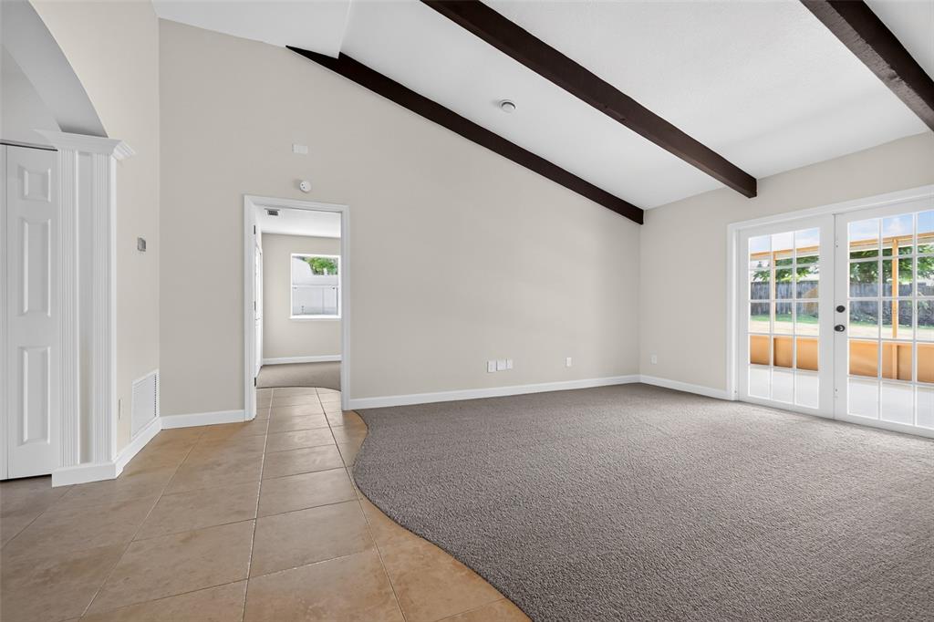 A living room features vaulted ceilings with dark beams, carpeted flooring, and French doors — 2221 ALEXANDER DRIVE, TITUSVILLE, FL