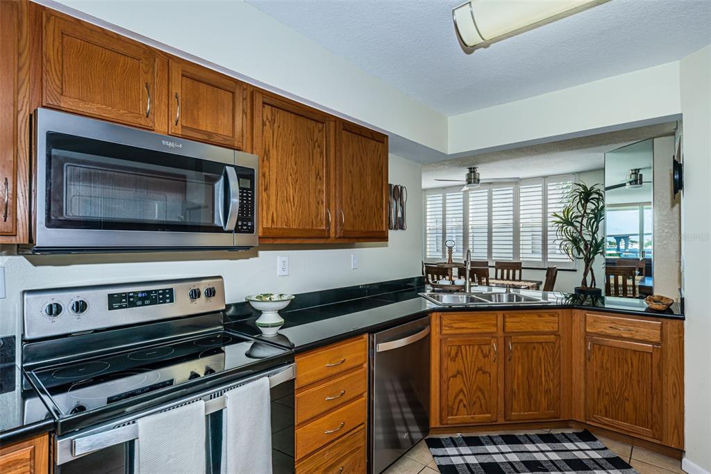 A kitchen features oak cabinets, black countertops, stainless steel appliances, and a view into a dining area — 6081 BAHIA DEL MAR CIRCLE UNIT 456, ST PETERSBURG, FL
