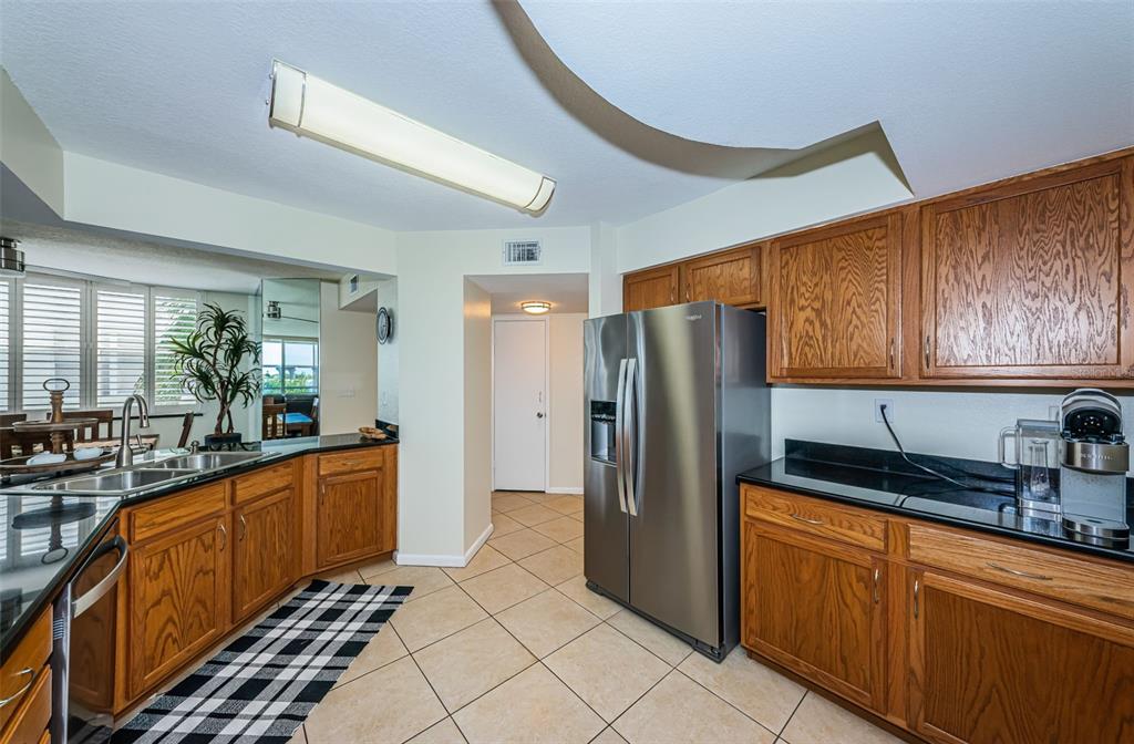 A kitchen features oak cabinets, black countertops, stainless steel appliances, and light-colored tile flooring — 6081 BAHIA DEL MAR CIRCLE UNIT 456, ST PETERSBURG, FL