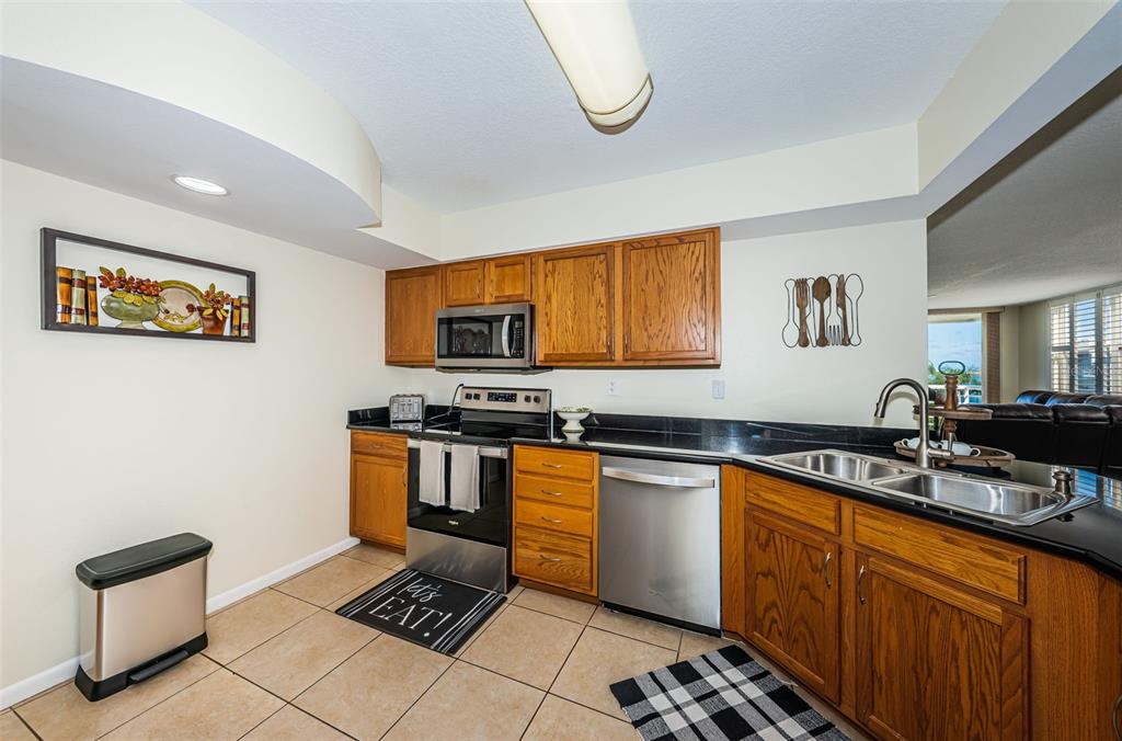 A kitchen features oak cabinets, black countertops, stainless steel appliances, and beige tile flooring — 6081 BAHIA DEL MAR CIRCLE UNIT 456, ST PETERSBURG, FL