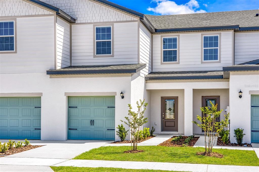 A two-story townhouse exterior features white stucco, light blue garage doors, and brown entry doors — 703 POPPY LANE, DUNDEE, FL