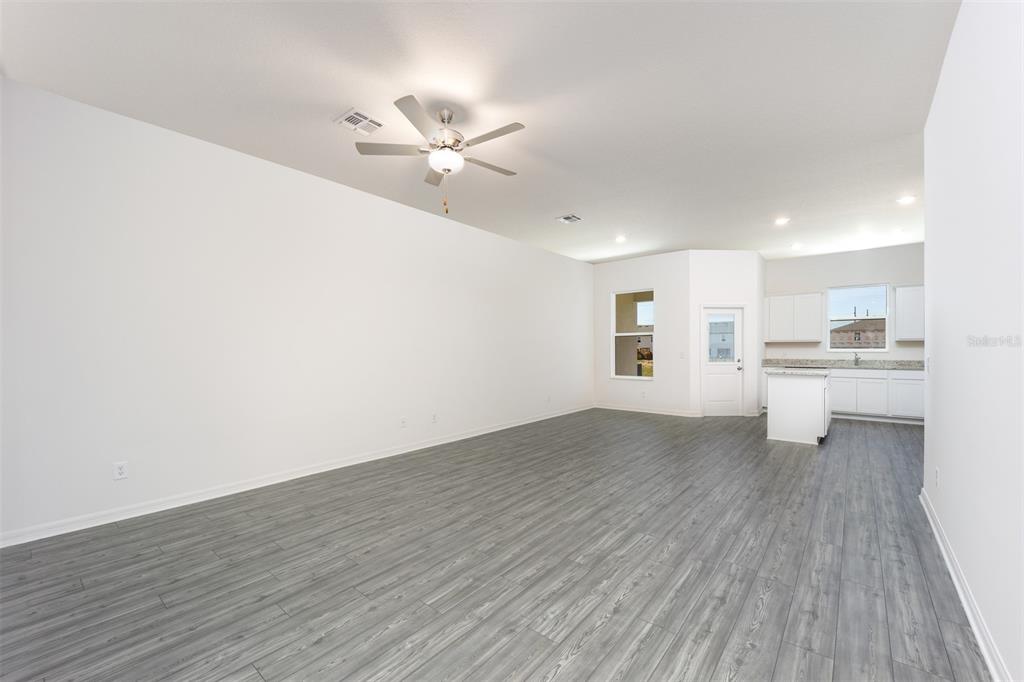 An open-concept living area features gray wood-look flooring, white walls, and an adjacent kitchen — 703 POPPY LANE, DUNDEE, FL