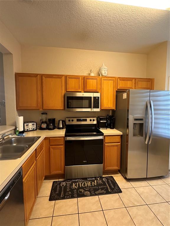 A kitchen features light wood cabinets, stainless steel appliances, and beige tile flooring — 141 LA MIRAGE STREET, DAVENPORT, FL