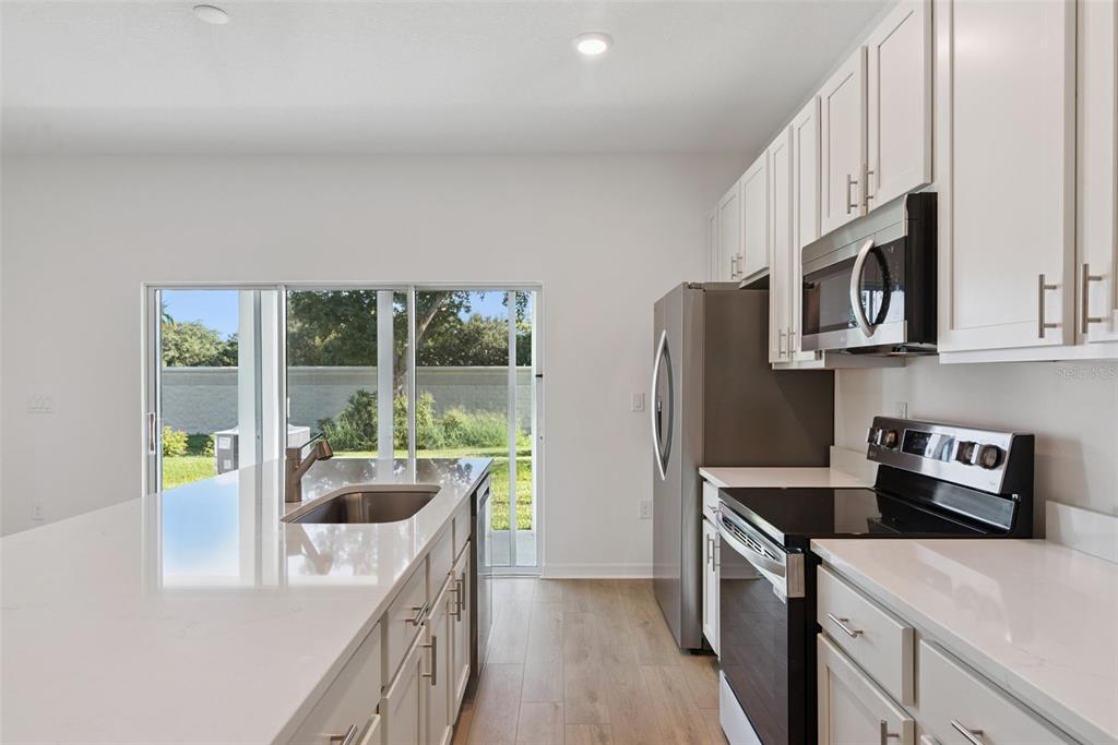 A modern kitchen features white cabinets, quartz countertops, stainless steel appliances, and a sliding glass door — 1108 CYPRESS ELM DRIVE, DELAND, FL