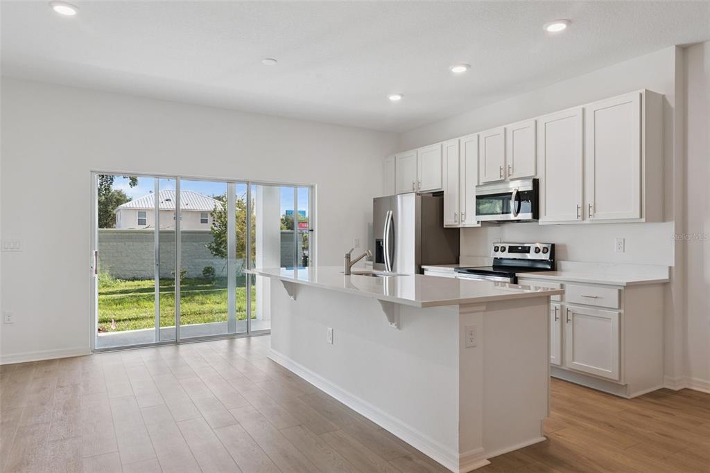 A modern kitchen features white cabinetry, stainless steel appliances, a quartz island, and sliding glass doors — 1108 CYPRESS ELM DRIVE, DELAND, FL