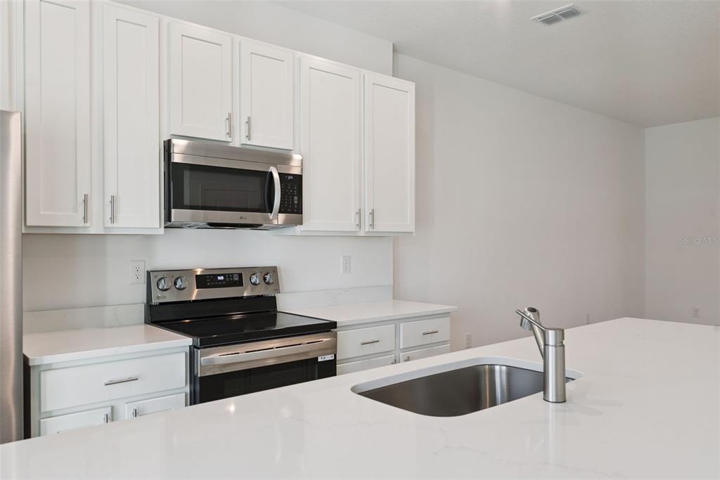 A modern kitchen features white cabinets, stainless steel appliances, and a white quartz island countertop — 1108 CYPRESS ELM DRIVE, DELAND, FL
