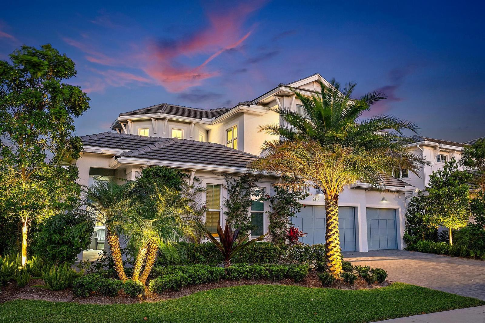 A two-story house with a gray tile roof, palm trees, and a paved driveway at dusk — 9338 Crestview Circle, Palm Beach Gardens FL 33412, PALM BEACH GARDENS, FL