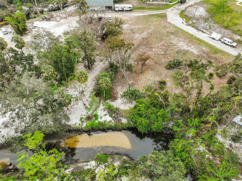 An aerial view shows a wooded lot with a small pond and a gravel driveway — 9423 BULLFROG COURT, GIBSONTON, FL