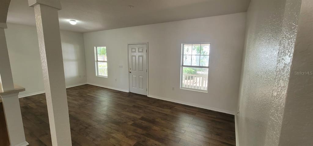 An empty room features wood-look flooring, white walls, two windows, and a central white door — 1004 PARK CENTRAL CIRCLE, GROVELAND, FL