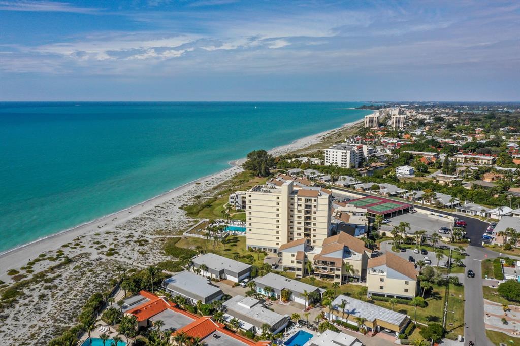 An aerial view shows a tall beachfront condominium building surrounded by smaller residential units — 700 GOLDEN BEACH BOULEVARD UNIT 236, VENICE, FL
