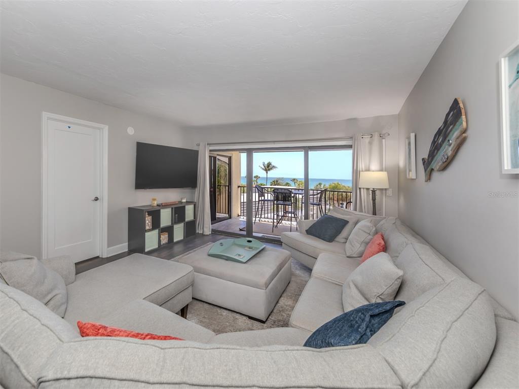 A living room features a large sectional sofa, a television, and a balcony with ocean views — 700 GOLDEN BEACH BOULEVARD UNIT 236, VENICE, FL