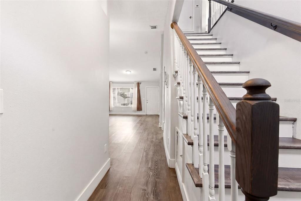 A hallway with wood-look flooring leads to a living area past a wooden staircase — 1254 SANDESTIN WAY, ORLANDO, FL