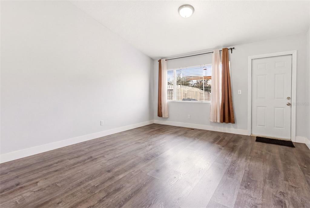 An empty room with light gray walls, wood-look flooring, a window with curtains, and a door — 1254 SANDESTIN WAY, ORLANDO, FL