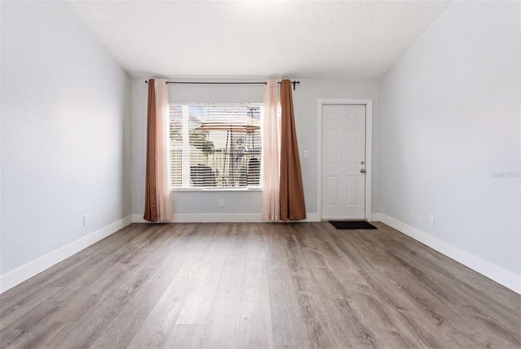 An empty room with light gray walls, wood-look flooring, a window with curtains, and a door — 1254 SANDESTIN WAY, ORLANDO, FL