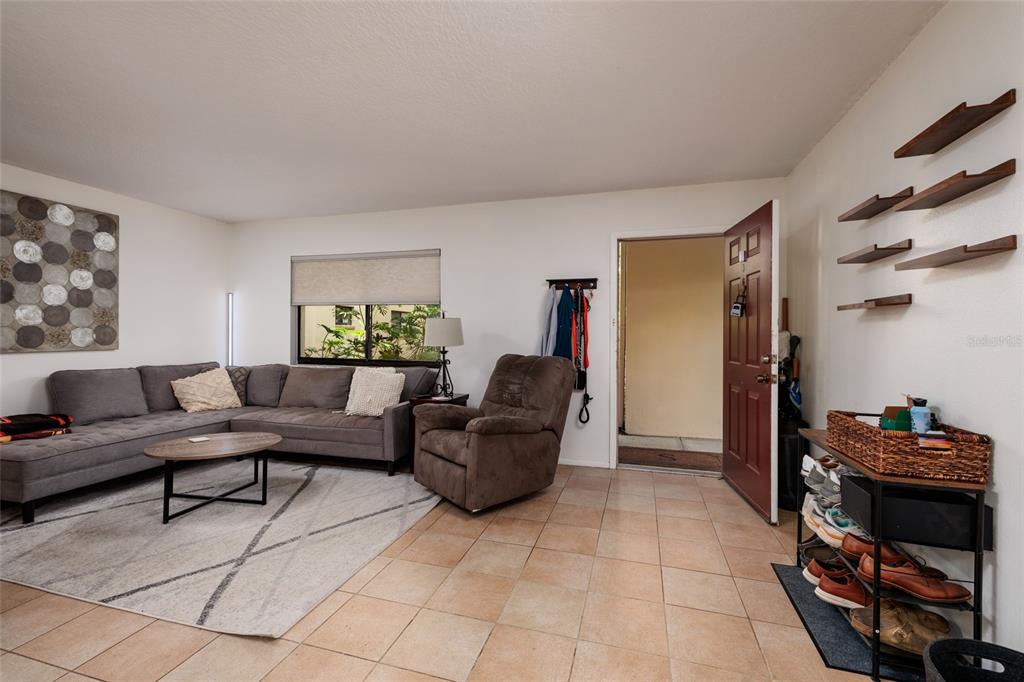 A living room features a grey sectional sofa, a recliner, tile flooring, and an entryway door — 11708 RAINTREE VILLAGE BOULEVARD UNIT A, TEMPLE TERRACE, FL
