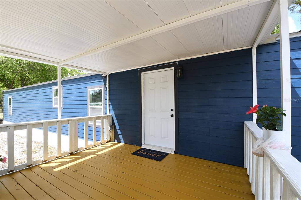 A covered wooden porch with white railings leads to a blue house with a white door — 7457 NE HIGHWAY 349, OLD TOWN, FL