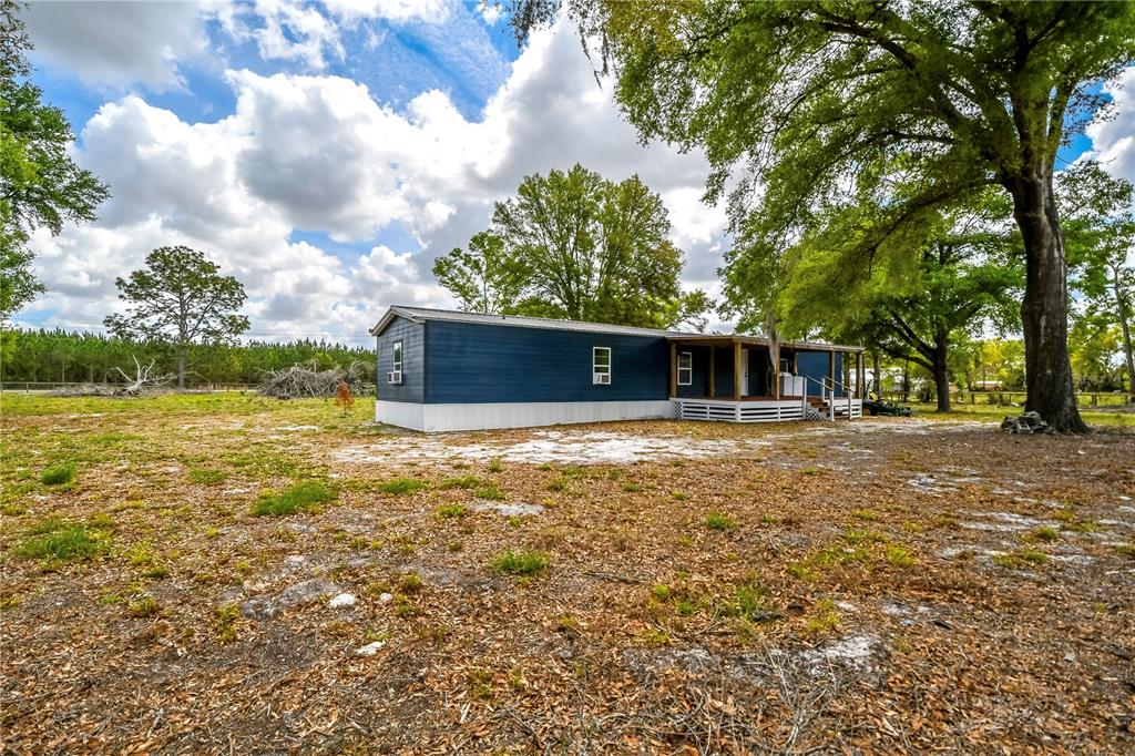 A blue manufactured home sits on a large, grassy lot with mature trees — 7457 NE HIGHWAY 349, OLD TOWN, FL