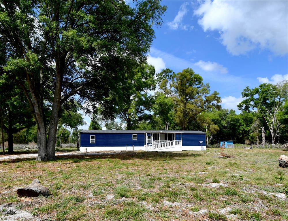 A blue mobile home with a white porch sits on a grassy, tree-filled lot — 7457 NE HIGHWAY 349, OLD TOWN, FL