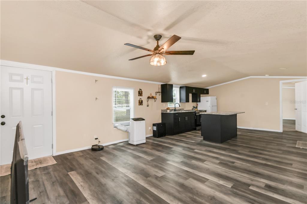 An open-concept living room and kitchen featuring dark cabinets, a kitchen island, and wood-look flooring — 7457 NE HIGHWAY 349, OLD TOWN, FL