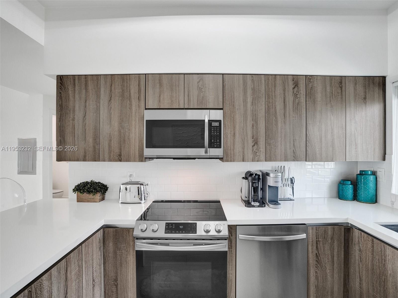 A kitchen features wood-grain cabinets, stainless steel appliances, white countertops, and a white subway tile backsplash — 601 NE 36th St # 1003, Miami FL 33137, MIAMI, FL
