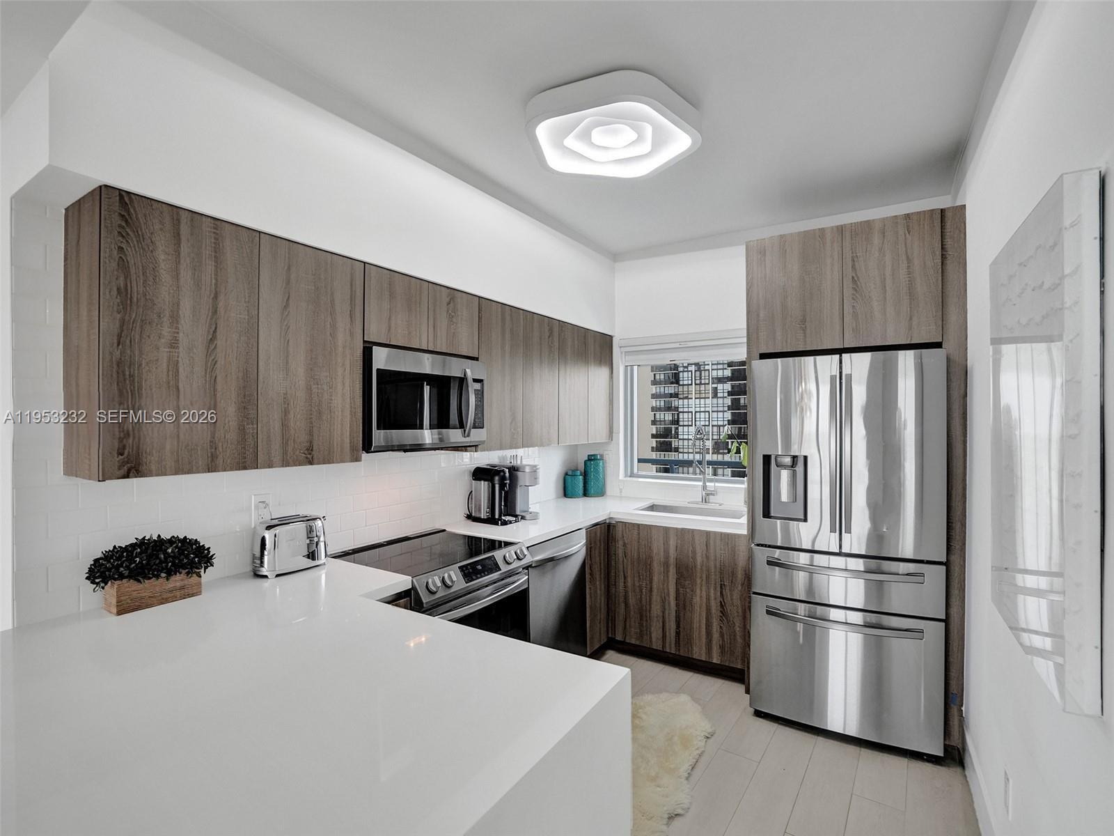 A modern kitchen features wood-grain cabinets, stainless steel appliances, and white quartz countertops — 601 NE 36th St # 1003, Miami FL 33137, MIAMI, FL