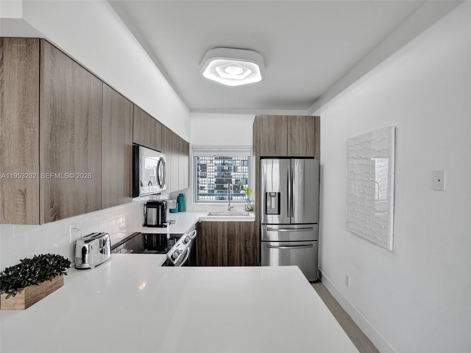 A modern kitchen features wood-tone cabinetry, stainless steel appliances, and white quartz countertops — 601 NE 36th St # 1003, Miami FL 33137, MIAMI, FL