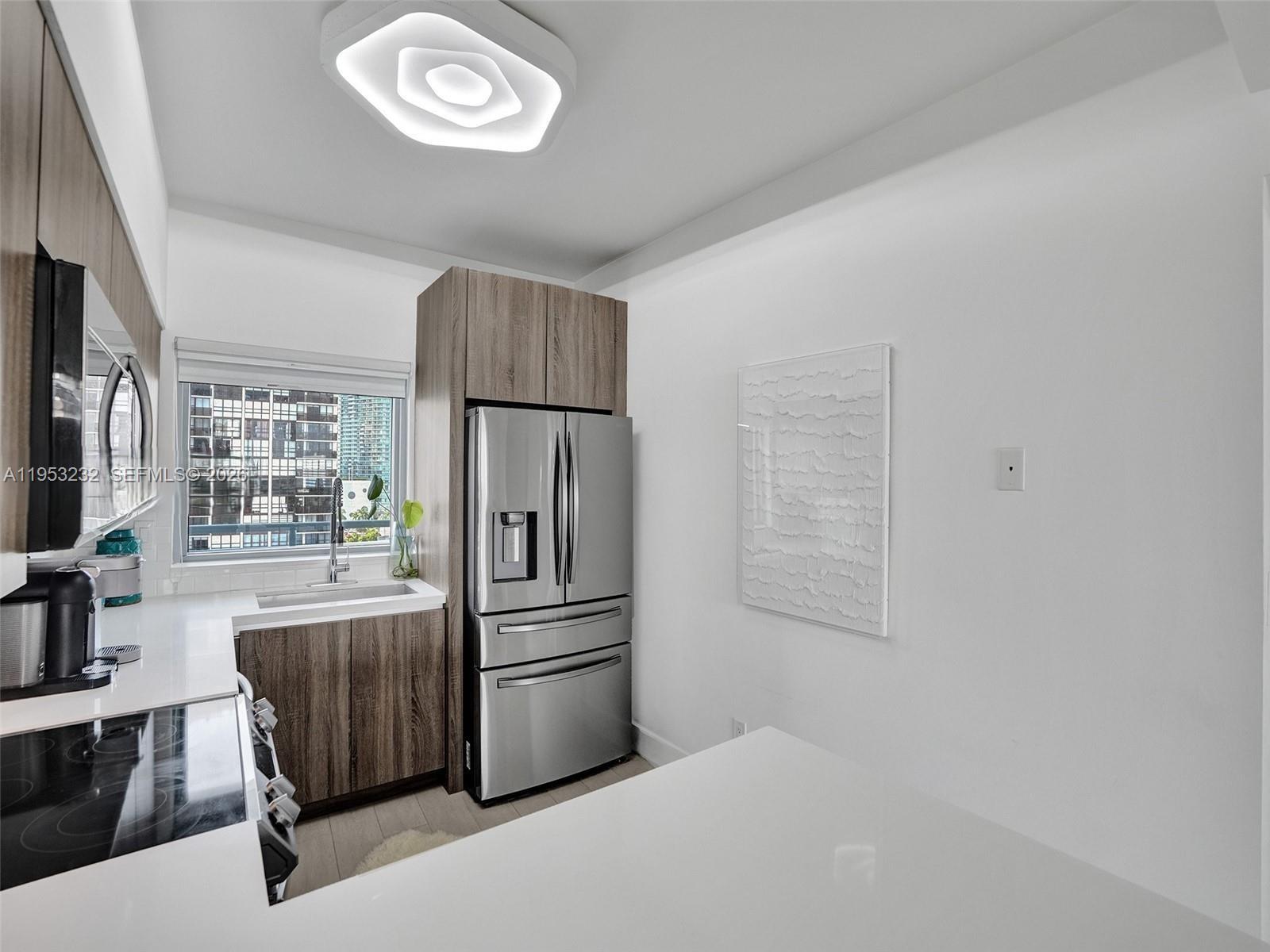 A modern kitchen features wood-toned cabinetry, stainless steel appliances, and a view of city buildings — 601 NE 36th St # 1003, Miami FL 33137, MIAMI, FL