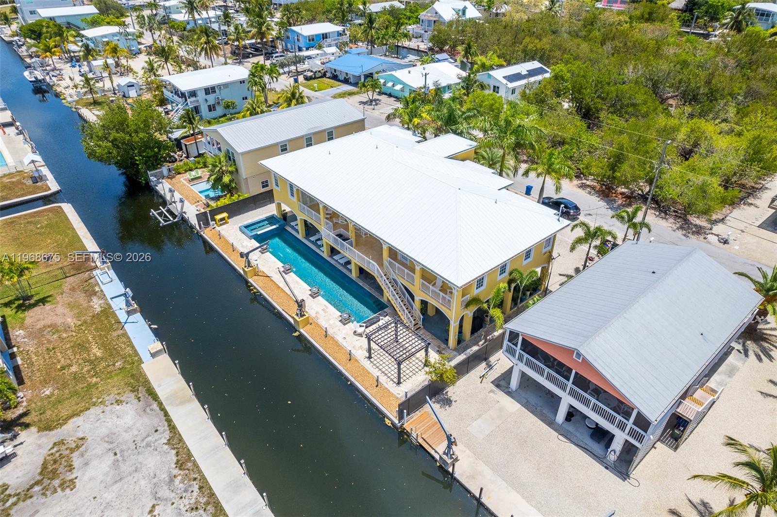 An aerial view shows a yellow house with a long pool beside a canal — 30825 Ortega Ln, Big Pine FL 33043, BIG PINE, FL