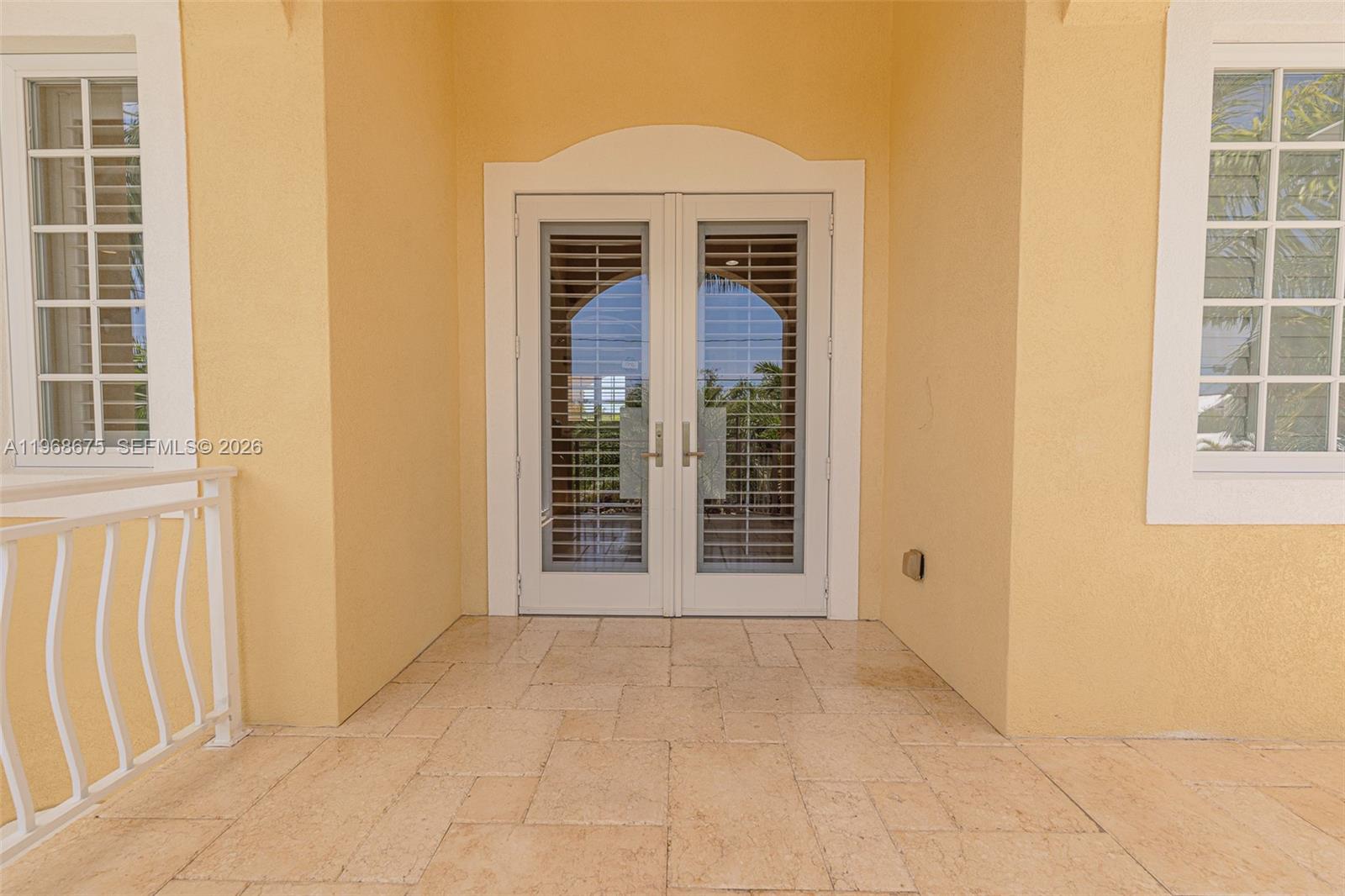 A covered patio features light-colored stone flooring and double glass doors with interior shutters — 30825 Ortega Ln, Big Pine FL 33043, BIG PINE, FL